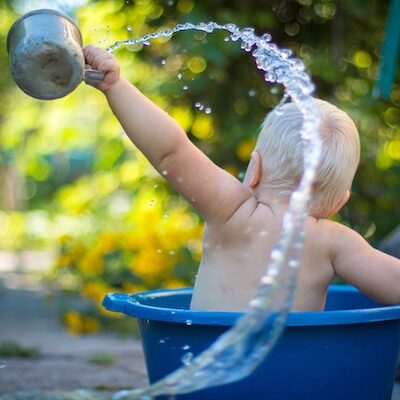 Photographie d'un jeune enfant jouant avec de l'eau assis dans une bassine bleue.