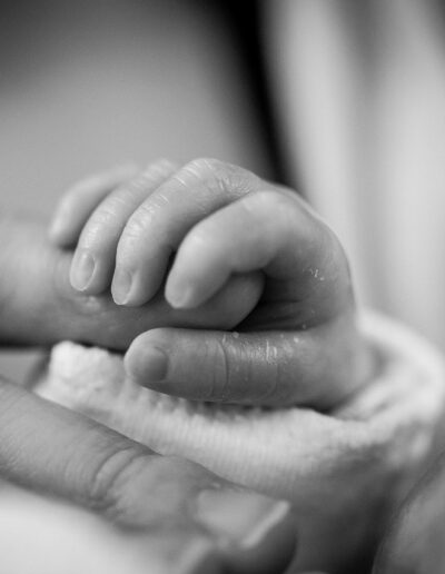 Photo d'une main de bébé tenant le doigt d'un adulte en noir et blanc.